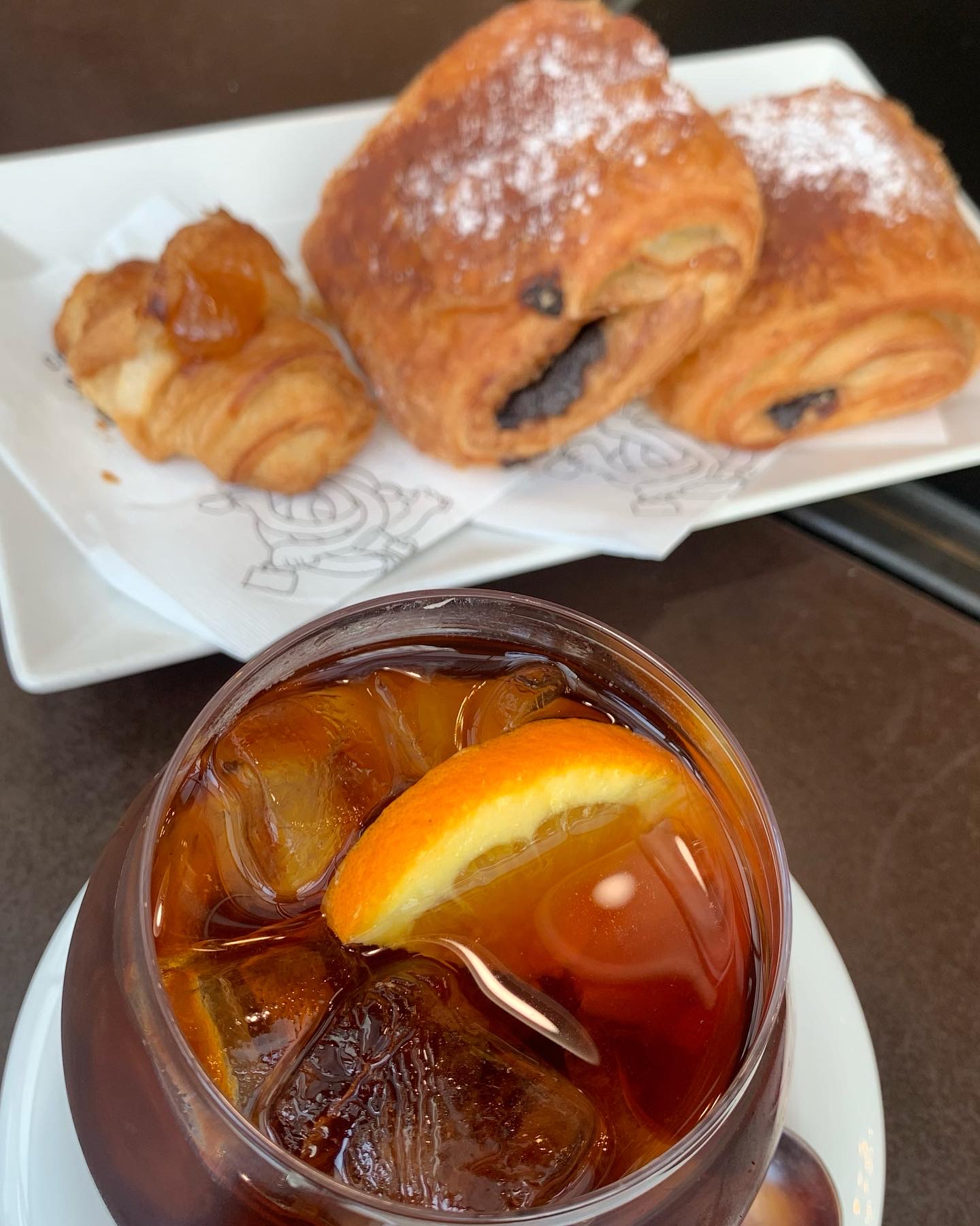 Pastry and iced black coffee with an orange slice.